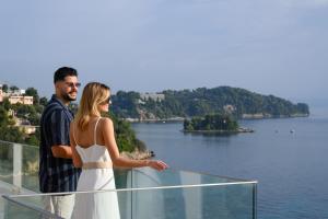 mężczyzna i kobieta stojący na balkonie z widokiem na jezioro w obiekcie Ray Hotel Corfu w mieście Perama