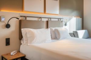 a white bed with white pillows and a phone on a table at Leonardo Hotel San Sebastián in Donostia-San Sebastián