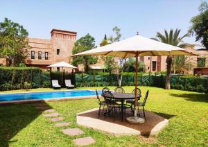 una mesa y sillas bajo una sombrilla junto a una piscina en Villa Ghali de Luxe & Golf, en Marrakech
