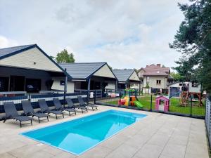 uma piscina com cadeiras e um parque infantil em Bursztynowo Domki Letniskowe em Ostrowo