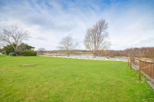 a large grassy field with a fence and a body of water at The Hideaway, 65 Salterns Beach Bungalows, Seaview in Seaview