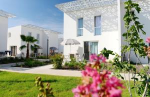 a white house with pink flowers in the foreground at Résidence Prestige Odalys Nakâra in Cap d'Agde