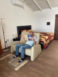 un hombre sentado en una silla en una habitación con una cama en Luxux Ferienwohnung Indepedencia Casa Blanca No.3, en Independencia