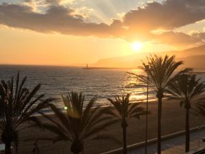 einen Sonnenuntergang über dem Meer mit Palmen am Strand in der Unterkunft Apartamento 1ª linea de mar in Almería