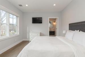 a white bedroom with a large white bed and windows at Villa Kimaal - Luxury with pool in Sag Harbor
