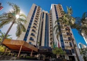 a tall building with palm trees in front of it at Sun Square Suítes Hotel By Lual in Goiânia