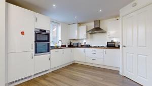 a white kitchen with white cabinets and a wooden floor at Tms Lovely 5-Bed House in Stanford-le-Hope in Stanford-le-Hope