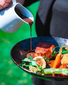 une personne versant de la sauce sur une assiette de nourriture dans l'établissement Mas De Baumes, à Ferrières-les-Verreries