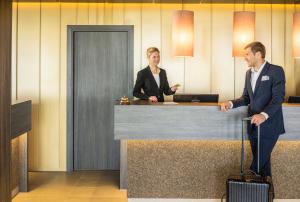 Dos hombres de traje están parados en un mostrador de recepción. en MYHOTEL München Olching, en Olching