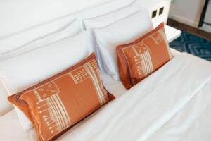 a white bed with two orange pillows on it at Shada Hotel - فندق شدا in Dubai