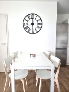 a white table and chairs with a clock on the wall at Le frontalier appart in Saint-Louis