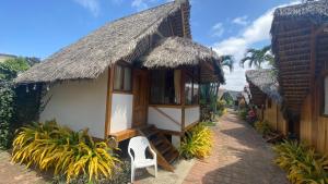 ein Haus mit einem Strohdach und einem Stuhl im Freien in der Unterkunft Zutalu - Playa Sur in Puerto López