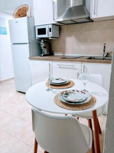 Una cocina blanca con una mesa con dos platos y vasos. en APARTAMENTO DE AMY CON VISTA AL MAR 2, en Huelva