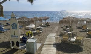 a surfboard on a beach with chairs and umbrellas at Little Octopus in Kalamaki Heraklion