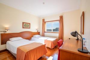 a hotel room with two beds and a desk at Hotel Ulveira in Oliveira de Frades