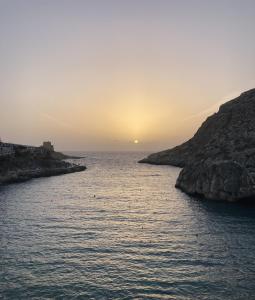 a sunset over a body of water next to a cliff at Seafront duplex Penthouse with Terrace overlooking Xlendi Bay in Xlendi
