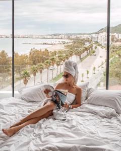 a woman sitting on a bed reading a book at Yacht Hotel in Vlorë