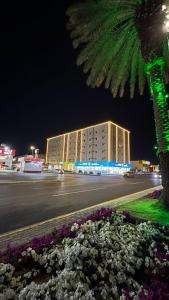 a building at night with a palm tree and flowers at رونزا للوحدات السكنية المفروشة Rwnza Hotel Apartments in Tabuk