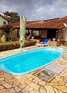 a blue swimming pool with a umbrella and a chair at Casa da Lua in São Pedro da Aldeia