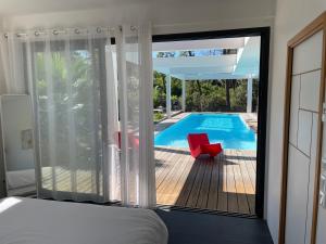 een slaapkamer met uitzicht op een zwembad en een rode stoel bij Villa CALIFORNIA Piscine chauffée 14x4m Abatilles Mouleau 10 pers in Arcachon