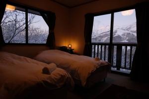two beds in a room with two large windows at WAKURABA- Chalet with the best views in Hakuba! in Hakuba