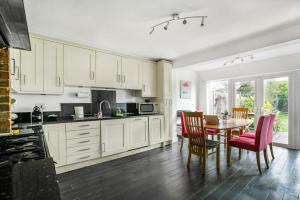 una cucina con armadi bianchi, tavolo e sedie di Gorgeous Cosy home 2 Miles from Heathrow Airport ad Ashford