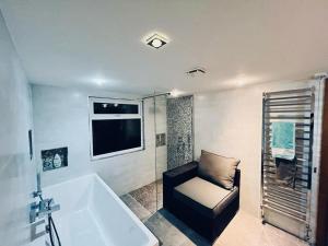 un bagno con vasca, sedia e finestra di Gorgeous Cosy home 2 Miles from Heathrow Airport ad Ashford