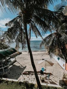 a palm tree on a beach with a chair and an umbrella at Gloria's Beach House in Oslob