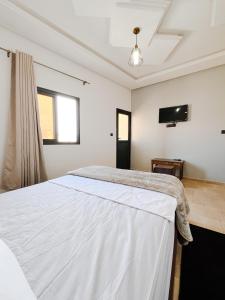a bedroom with a white bed and a flat screen tv at Hotel Ahmed Ali in Dakhla