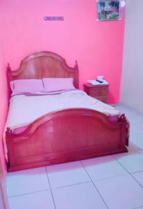 Cama en habitación rosa con marco de madera en HOSTAL EL CASTILLO SIGCHOS, en Sigchos