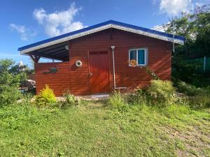a wooden cabin with a red door in a field at Bungalows Mathilde-non fumeur in Bouillante