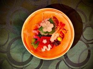 an orange bowl of food with vegetables on a table at Sarusawaike Yoshidaya in Nara