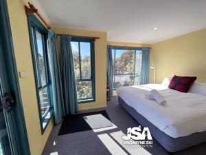 a bedroom with a bed and two large windows at Naturescape in Jindabyne