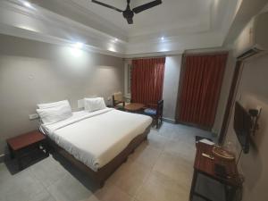 a bedroom with a large white bed and a television at Hotel Pulikeshi in Bangalore