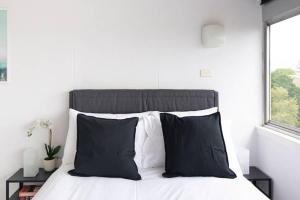 a bed with black and white pillows and a window at Studio with Stunning Views and Free Parking in Sydney
