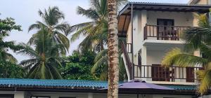 un edificio blanco con palmeras y sombrilla en Thiranagama Beach Hotel, en Hikkaduwa