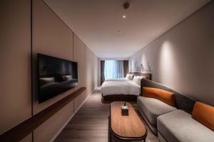 UrCove by Hyatt Shanghai Lujiazui Expo Center في شانغهاي: غرفة فندق بسرير واريكة وتلفزيون