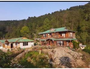 Hilltop Rabong Resort, Sikkim في Ravangla: منزل خشبي كبير مع سقف أخضر على تلة
