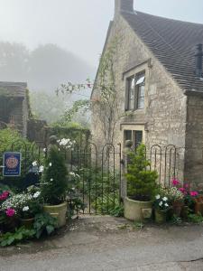 an old stone house with a gate and flowers at Dove Cottage in Bisley