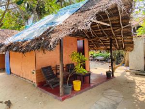 Cabaña pequeña con techo de paja y silla en Rainbow Village Cabanas, en Arugam Bay