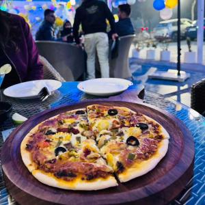 a pizza sitting on top of a wooden plate on a table at Hotel Imperial Park in Gurgaon