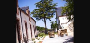 a courtyard with two wooden chairs and a tree at Logis Hôtel La ferme du Blanchot in Crossac