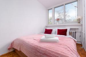 a white bedroom with a pink bed with red pillows at Zielińskiego Colourful Apartment in Wrocław