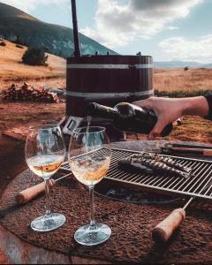two glasses of white wine next to a grill at Barrel Land Blidinje - Drvena bačva za spavanje in Posušje