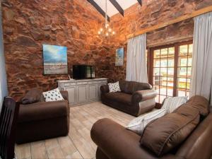 sala de estar con muebles de cuero y pared de piedra. en Crooked Cottage, en Pelindaba