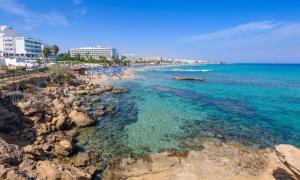 a beach with blue water and rocks and buildings at Green Bay Villa #15 in Protaras