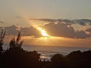um pôr-do-sol sobre o oceano com o sol escondido atrás das nuvens em Utopia in Palm Beach em Port Edward