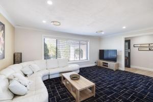 a living room with a white couch and a tv at Spacious House with Pool - 5 min walk to Lake in Wyong
