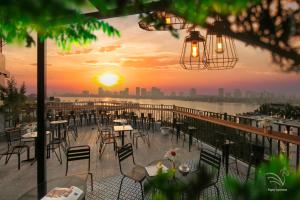 ein Restaurant mit Tischen und Stühlen auf einem Balkon mit Blick auf den Sonnenuntergang in der Unterkunft Westlake Pearl Apartment & Hotel - By Pegasy Group in Hanoi