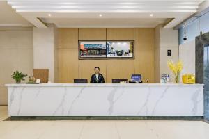 City Comfort Inn Kunming Dashuying Yejin Hospital Wangdaqiao في كونمينغ: رجل يجلس في مكتب الاستقبال في بهو الفندق
